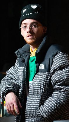 a man with glasses and a hat is looking at the camera while wearing a jacket