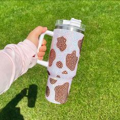 a person holding a coffee cup in their hand on the grass with an animal print