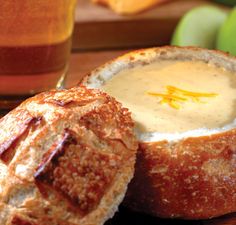 a close up of a bread bowl filled with soup next to an apple and some other fruit