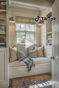 a window seat with pillows and blankets on it in front of a book shelf filled with books