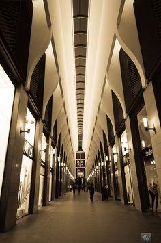 people are walking through an indoor mall with lights on either side of the walkway and ceiling