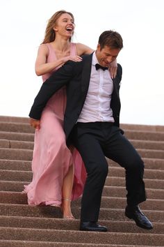 a man in a tuxedo and a woman in a pink dress sitting on some steps