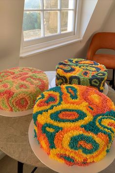 three colorful cakes sitting on top of a table next to each other in front of a window