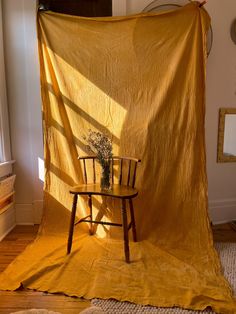 a chair sitting in front of a yellow sheet on top of a wooden table next to a window