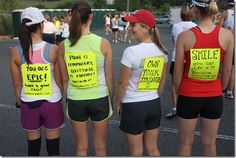 three girls with signs on their backs standing in a parking lot, one holding a tennis racket and the other wearing shorts