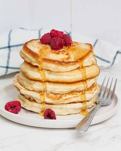 a stack of pancakes with syrup and raspberries on a plate next to a fork