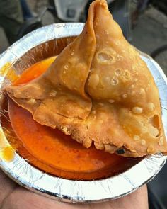 a hand holding a metal plate with food in it and sauce on the side,