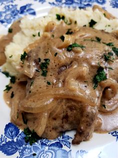 meat and gravy on a blue and white plate with mashed potatoes, parsley