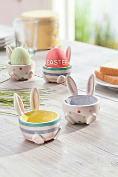 three ceramic bowls with painted easter bunnies in them on a table next to bread