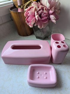 pink bathroom accessories sitting on a counter next to a vase with purple flowers in it