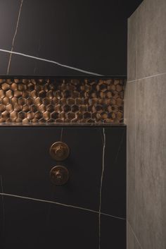 a black and gold tiled shower stall with two brass knobs on the wall next to it