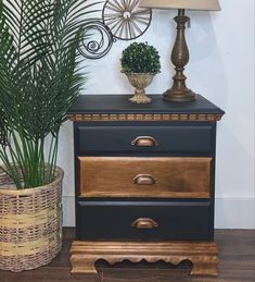 a black and gold chest of drawers next to a lamp with a green plant on top