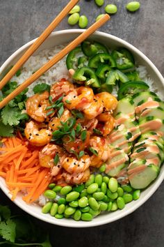 a bowl filled with rice, shrimp and vegetables next to chopsticks on the side