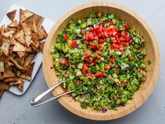 a wooden bowl filled with chopped vegetables next to a cutting board and serving utensils