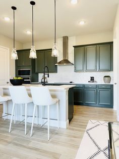 a kitchen with dark green cabinets and white counter tops, three bar stools in front of the island