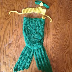 a green knitted mermaid tail and hat on a wooden floor with a string attached to it