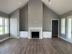 an empty living room with gray walls and white trim on the fireplace, hardwood floors