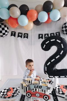 a young boy sitting in front of a birthday cake at a race car themed first birthday party