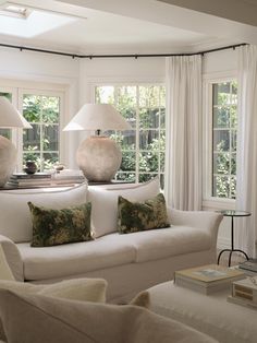 a living room filled with white furniture and two lamps on top of the windows sill