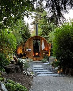 a small wooden cabin in the middle of some trees and bushes with lights on it