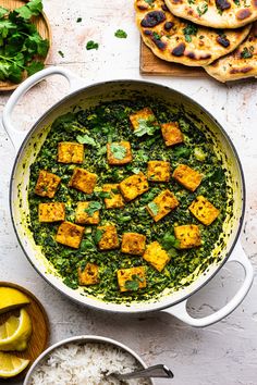 a pan filled with tofu and spinach on top of rice next to sliced lemons