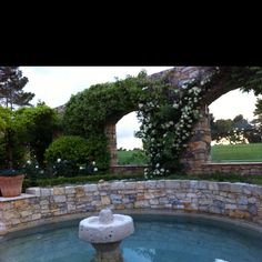 an outdoor fountain in the middle of a stone walled area with flowers growing on it