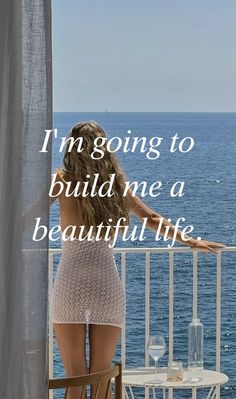 a woman standing on a balcony looking out at the ocean with her back to the camera