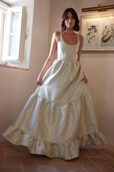 a woman in a white dress standing next to a window with a painting on the wall behind her