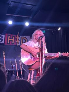 a woman singing into a microphone while holding a guitar in front of an audience at a concert