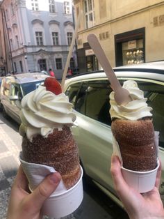 two ice cream sundaes with strawberries on top in front of a car