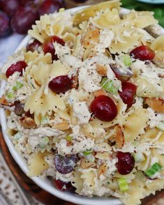 a white bowl filled with pasta salad on top of a wooden table next to grapes