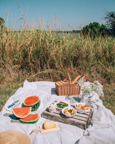 a picnic with watermelon, cheese and bread on a blanket in the grass