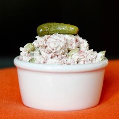 a white bowl filled with food sitting on top of an orange tablecloth next to a green pickle