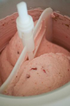 a close up of a blender filled with pink colored food and a white plastic bottle