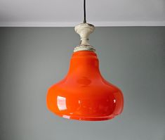 an orange light hanging from a ceiling in a room with gray walls and flooring