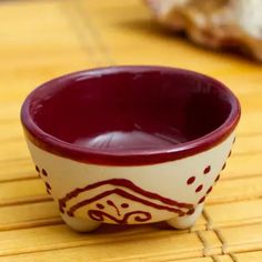 a small red and white bowl sitting on top of a bamboo mat next to a rock