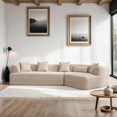 a living room with white walls and wood flooring is pictured in this image, there are two framed pictures on the wall above the couch