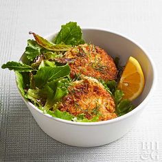 a white bowl filled with salad and meat on top of a table next to an orange slice