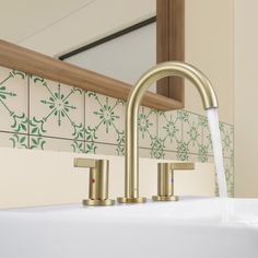 a faucet running water from a sink in a bathroom with green tiles on the wall