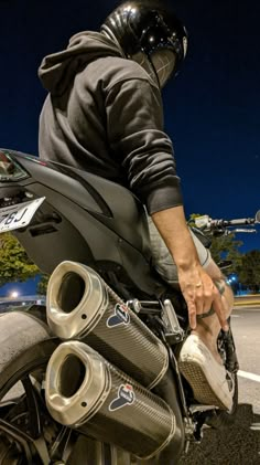 a man riding on the back of a motorcycle wearing a helmet and holding onto his exhaust pipe