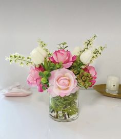 a vase filled with pink and white flowers on top of a table next to a candle