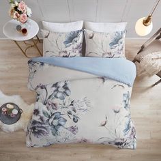 a bed with blue and white floral comforter set on top of it next to a table