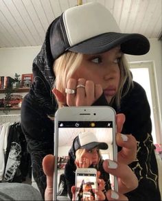 a woman taking a selfie with her cell phone while wearing a baseball cap and jacket