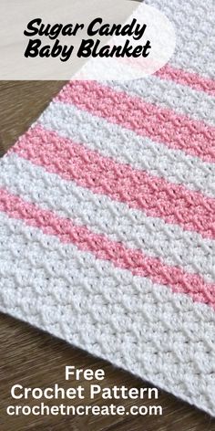 a crocheted baby blanket with pink and white stripes on the bottom, sitting on top of a wooden table