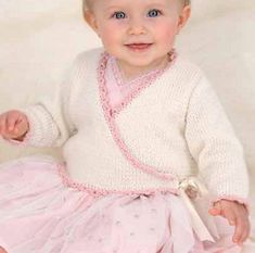 a baby in a pink dress sitting on a white blanket