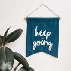 a blue banner that says keep going hanging on a wall next to a potted plant