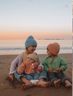 two women and one child sitting on the beach at sunset or sunrise with their feet in the sand