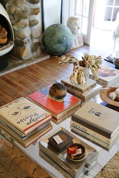 a coffee table topped with lots of books on top of a wooden floor next to a fire place