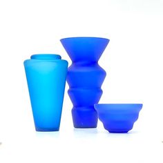 three blue vases and one bowl on a white surface