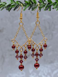 gold plated earrings with red glass beads hanging from the ends of chains on a tree branch